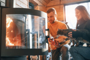 Man putting wood into the fireplace Woman is sitting with cute cat