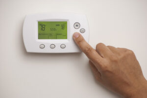 Male hand on digital thermostat set at degrees